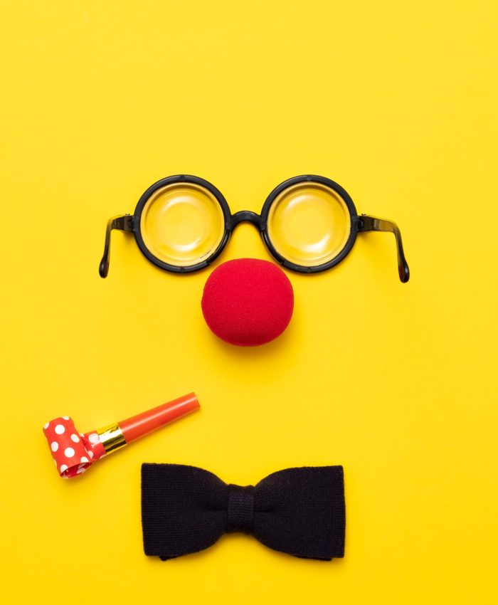 Funny glasses, a red clown nose and tie on a colored background, like a face. Flat lay. Funny costume for the holidays. Anonymous concept.